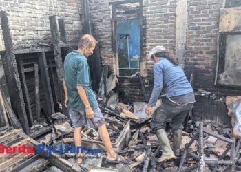 Abdul Rohman (67), perajin kerupuk asal Baleharjo, Pacitan, bersama seorang warga menyusuri puing-puing rumah produksinya yang hangus dilalap api, Selasa (22/7/2025). Seluruh peralatan usaha miliknya ludes terbakar dalam insiden tersebut. (Foto: Sunardi/BeritaPacitan.com)