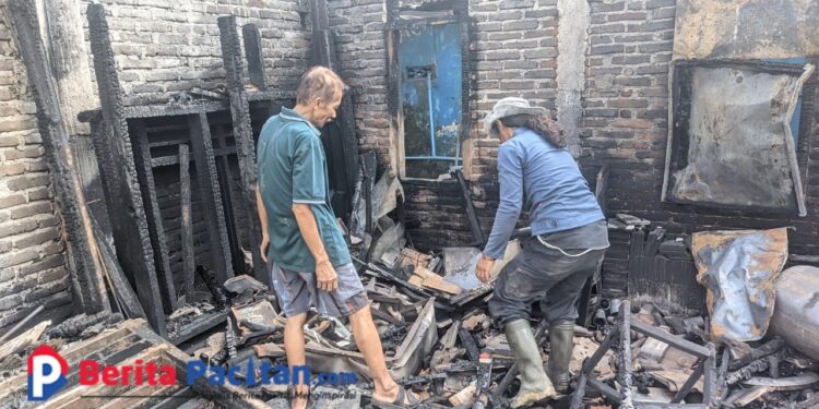 Abdul Rohman (67), perajin kerupuk asal Baleharjo, Pacitan, bersama seorang warga menyusuri puing-puing rumah produksinya yang hangus dilalap api, Selasa (22/7/2025). Seluruh peralatan usaha miliknya ludes terbakar dalam insiden tersebut. (Foto: Sunardi/BeritaPacitan.com)