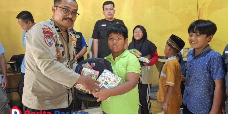 Bhabinkamtibmas Polsek Pacitan, Aipda Latip Utomo, menyerahkan bantuan perlengkapan sekolah kepada salah satu anak di Desa Kalikuning dalam kegiatan sosial yang digelar LSM Kalikuning Sigap Bersinergi (KSB). (Foto : Sunardi Berita Pacitan).