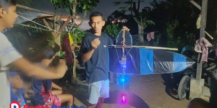 Pemuda di Desa Klesem, Kecamatan Kebonagung, tengah merakit layangan malam berlampu warna-warni. Tradisi musim angin ini tidak hanya menjadi hiburan, tetapi juga sarana mempererat kebersamaan lintas generasi di Pacitan. (Foto: Sunardi Berita Pacitan).