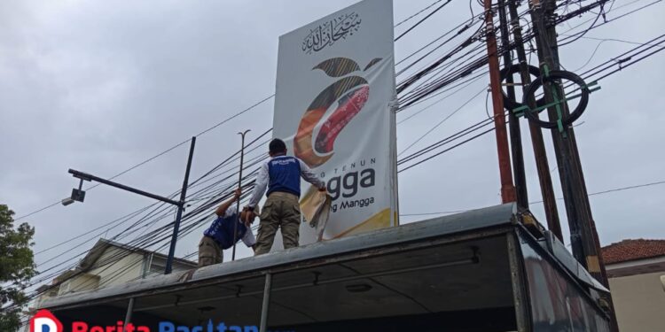 Petugas Satpol PP Pacitan saat menurunkan salah satu reklame tidak berizin dalam rangkaian penertiban di wilayah kota. (Foto: Sunardi/Berita Pacitan).