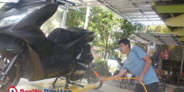 Seorang pekerja mencuci sepeda motor pelanggan di layanan cucian motor dan mobil milik Choirul Anam di Jalan Cut Mutia No. 01, Kelurahan Ploso, Pacitan, Senin, 19 Januari 2026. (Foto: Sunardi/Beritapacitan.com)