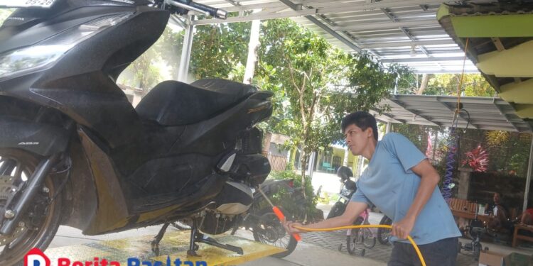 Seorang pekerja mencuci sepeda motor pelanggan di layanan cucian motor dan mobil milik Choirul Anam di Jalan Cut Mutia No. 01, Kelurahan Ploso, Pacitan, Senin, 19 Januari 2026. (Foto: Sunardi/Beritapacitan.com)